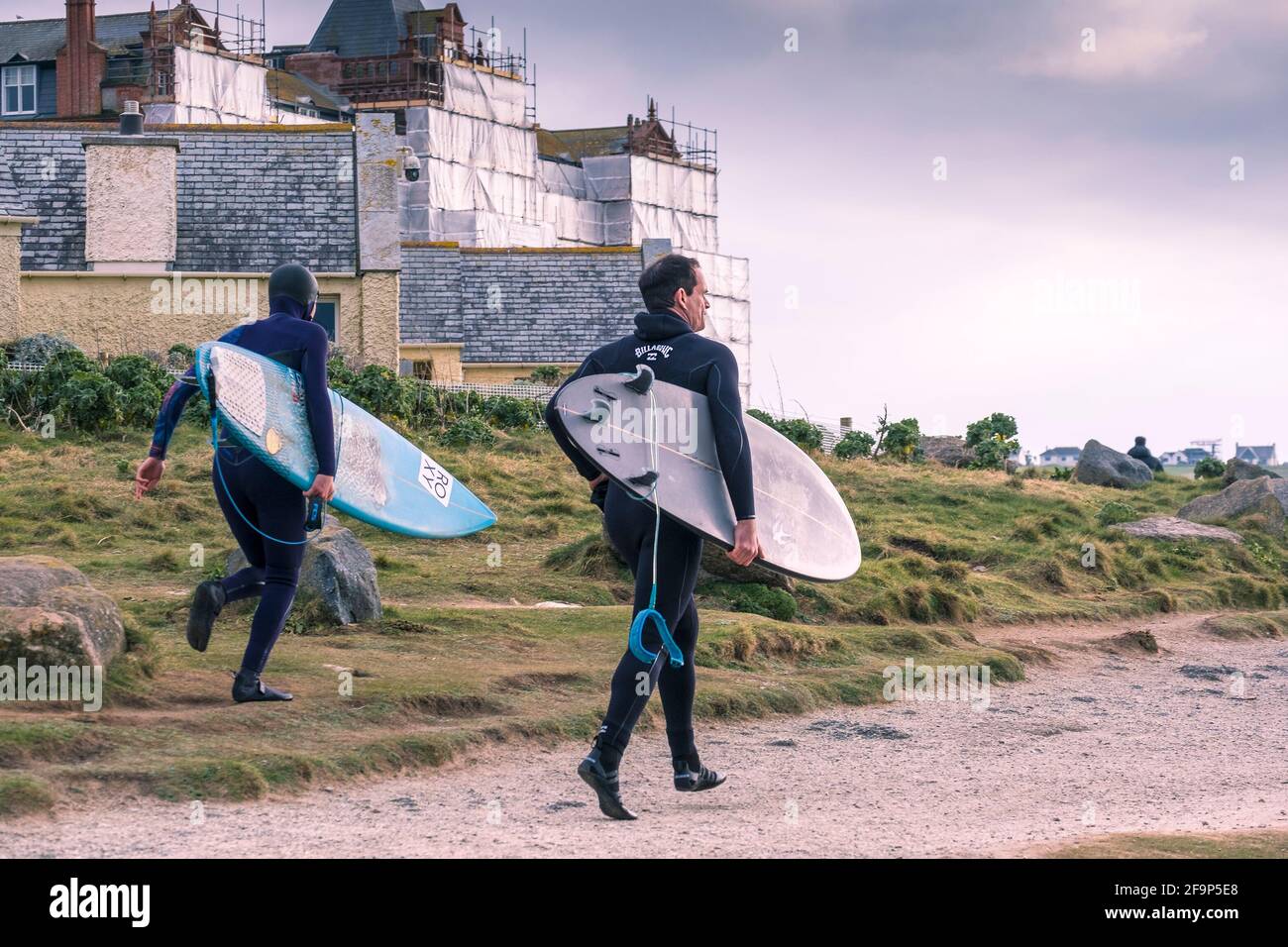 Deux surfeurs passionnés transportant leurs planches de surf et courant le long de la voie côtière sur la côte de Fistral à Newquay en Cornouailles. Banque D'Images