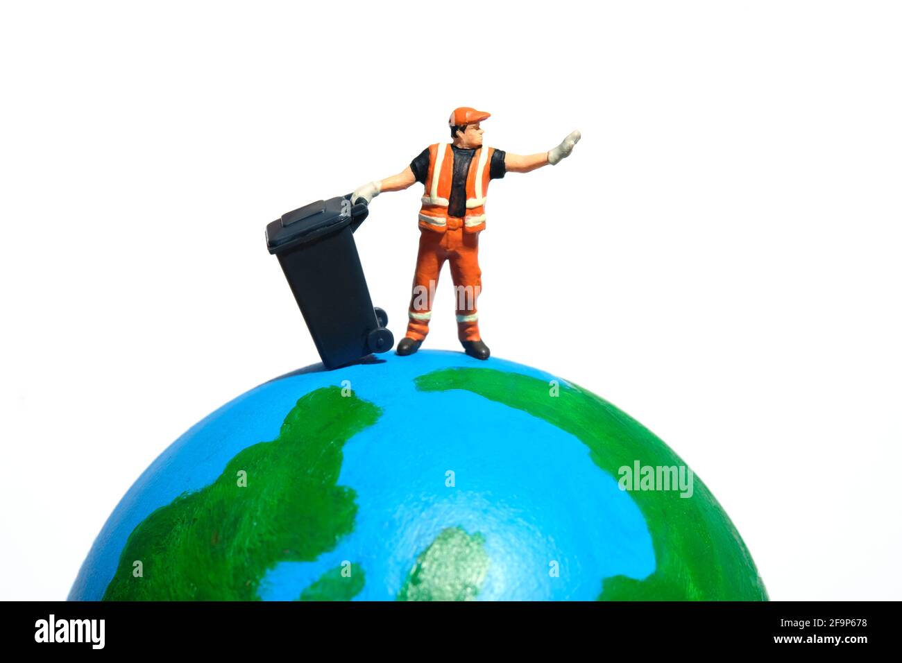 Travailleur de nettoyage avec une poubelle au-dessus du globe terrestre. Concept global de déchets. Photographie miniature de personnage Banque D'Images