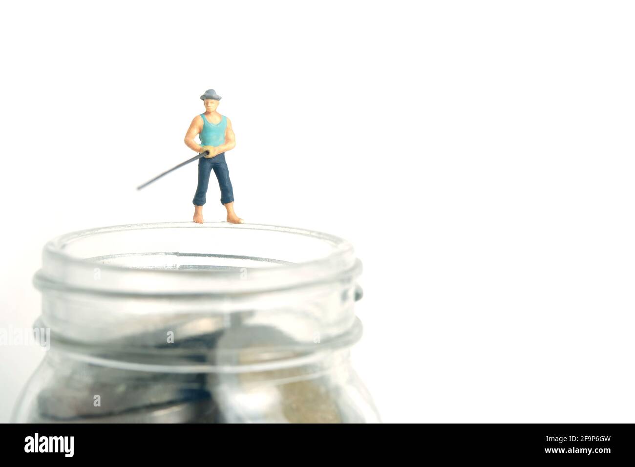 Photographie miniature de jouets de personnes. Un pêcheur à la ligne se tenant au-dessus de pot d'argent de la pièce de pêche. Isolé sur fond blanc. Banque D'Images