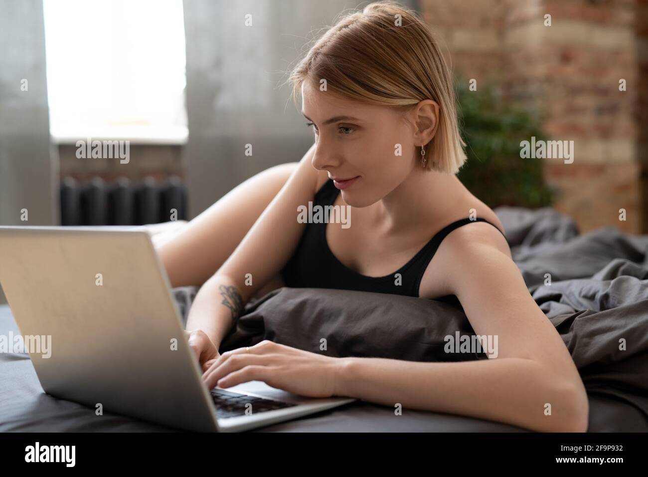 Jeune femme allongé sur le lit et tapant sur l'ordinateur portable elle travailler en ligne à la maison Banque D'Images