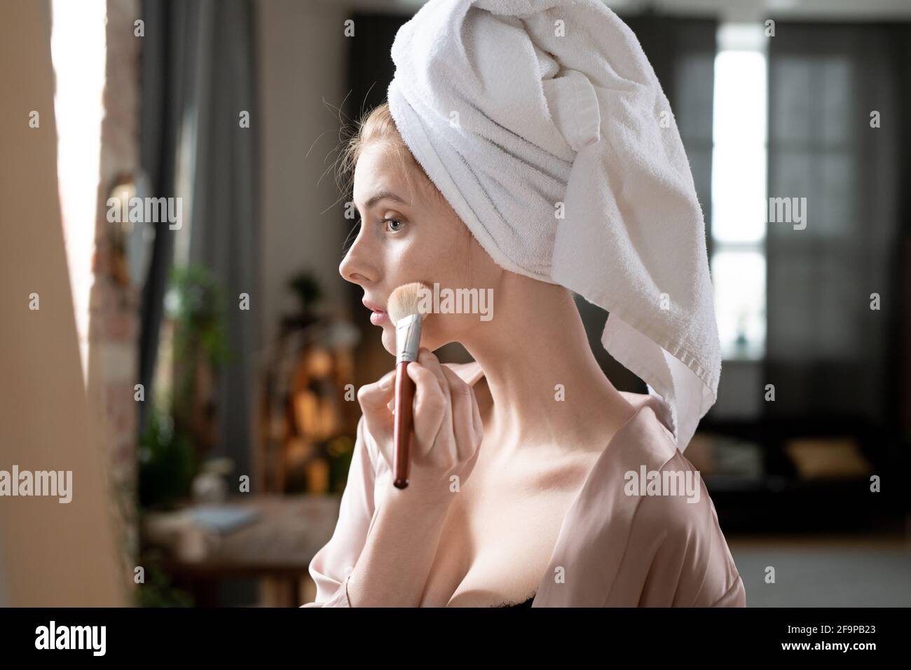 Jeune femme appliquant du maquillage sur son visage avec une brosse à maquillage devant le rétroviseur Banque D'Images