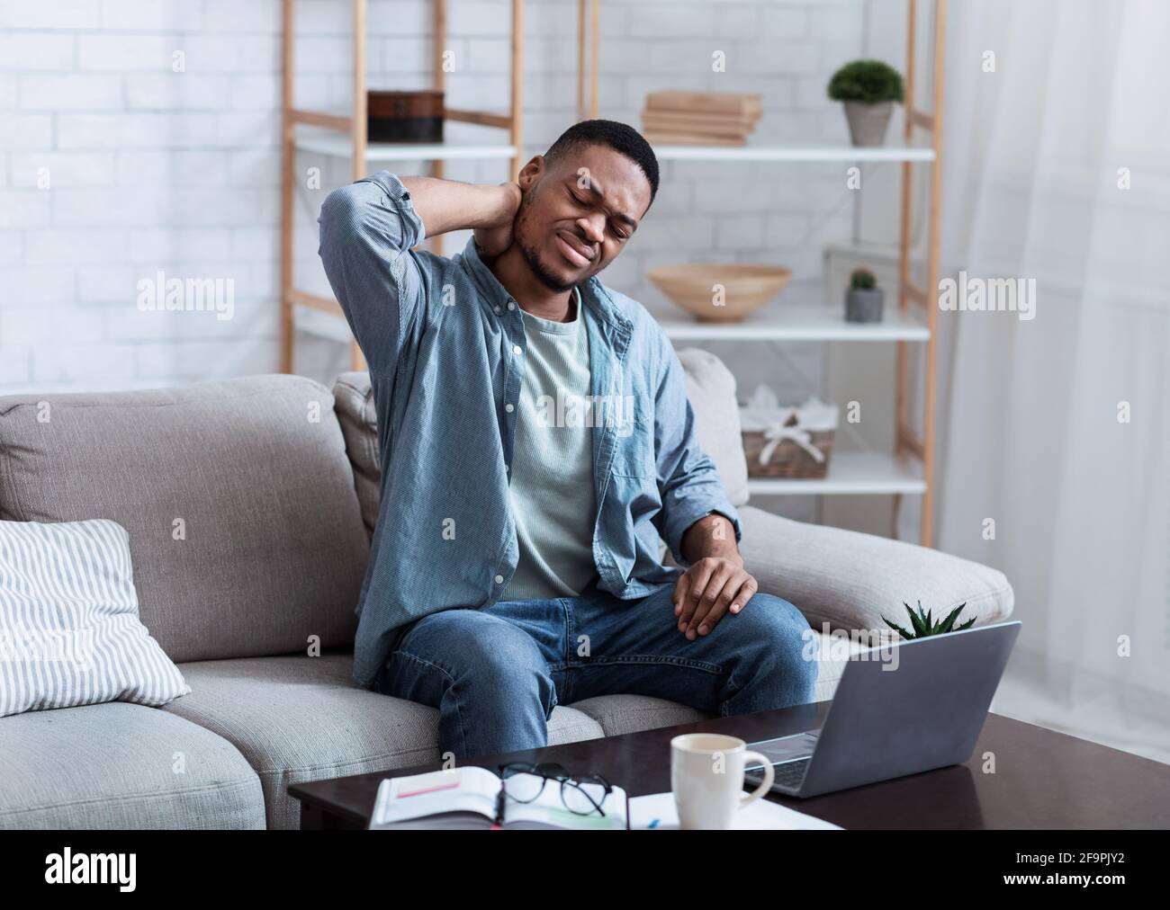 Homme afro-américain massant cou assis à l'intérieur d'ordinateur portable Banque D'Images