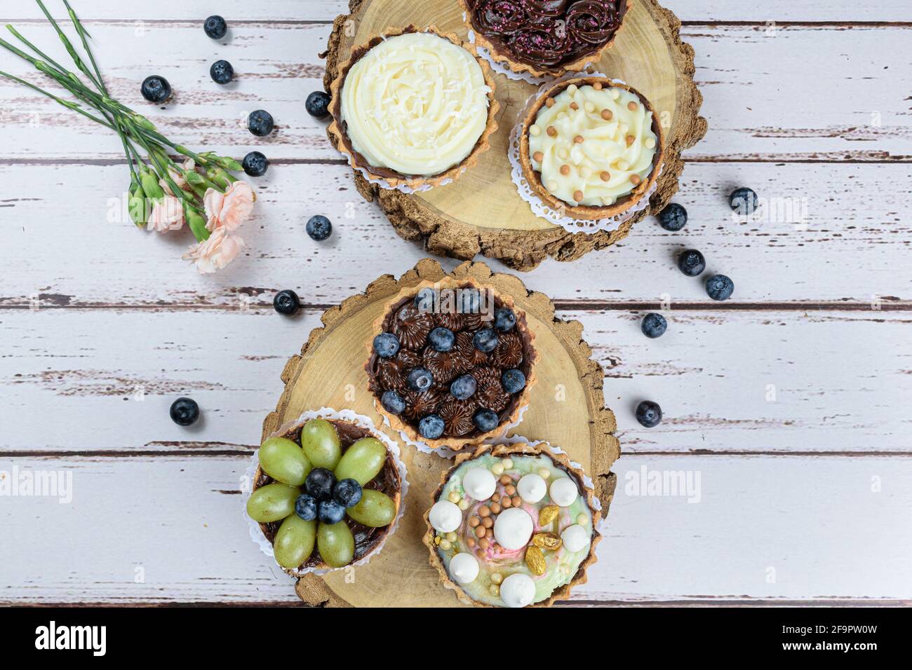 Tarte à la pâte de beurre farcie de ganache au chocolat, décorée de mertilos. Sur une plaque en bois et entourée d'autres tourtes et roses. Banque D'Images