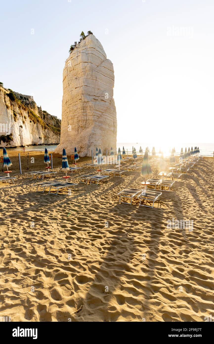 L'emblématique formation rocheuse Pizzomunno et chaises longues à l'aube, plage de Castello, Vieste, province de Foggia, Gargano, Apulia, Italie Banque D'Images
