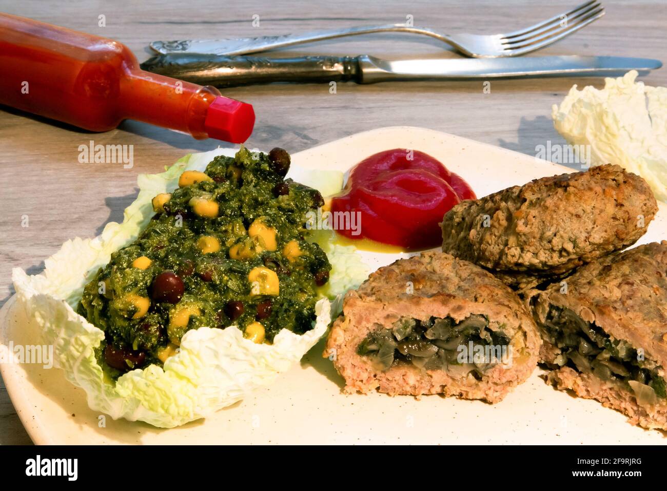 Côtelettes de bœuf avec garniture aux champignons, salade de légumes et ketchup servies sur une assiette légère avec une petite bouteille de sauce épicée couchée à côté Banque D'Images