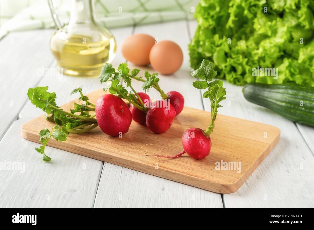 Humidifier des radis entiers avec des feuilles vertes sur une planche à découper en bois sur une table blanche. Ingrédients pour la salade de légumes de printemps crus avec des œufs. Faibles calories Banque D'Images