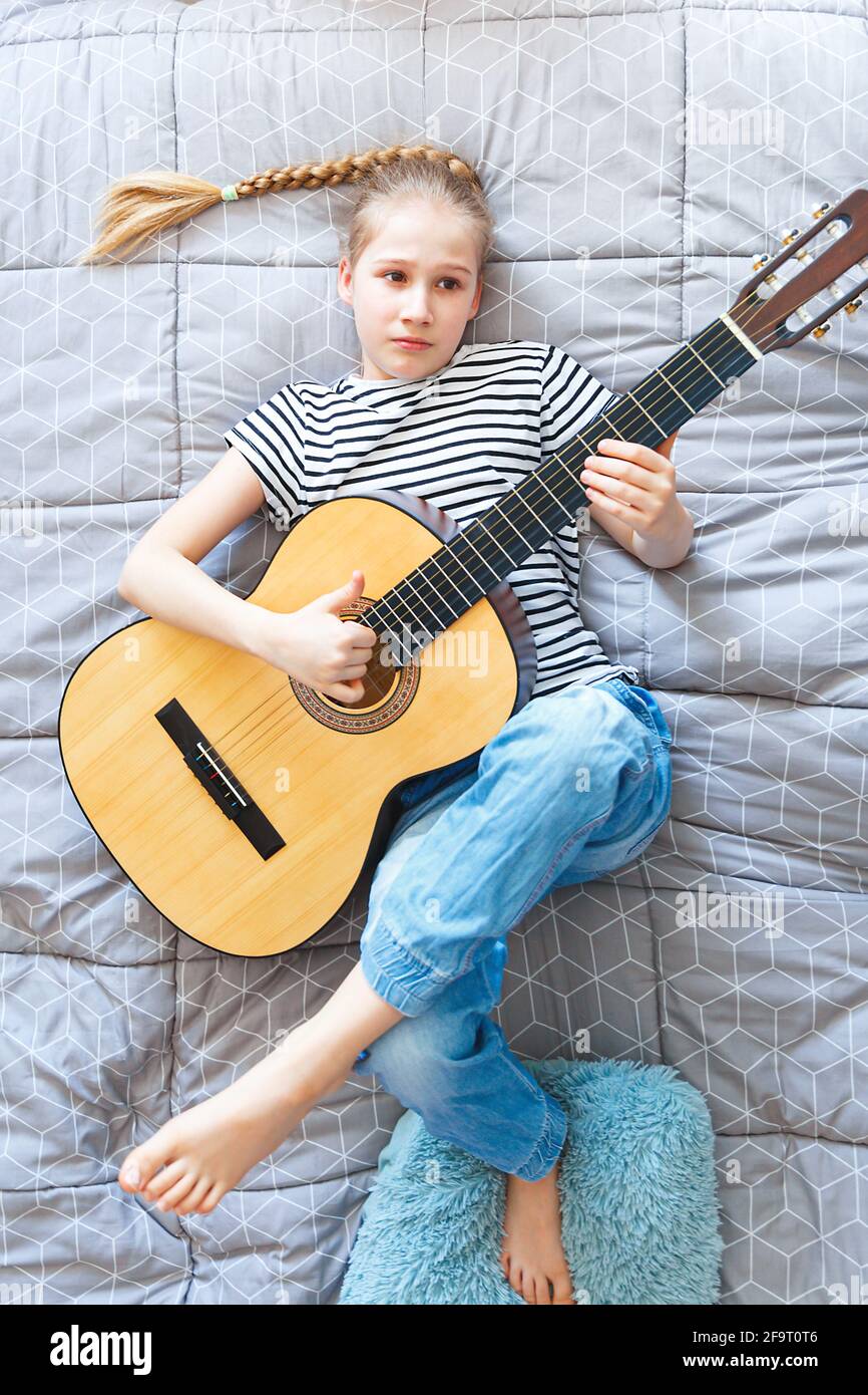 Triste fille jouant de la guitare acoustique à la maison, allongé sur le lit, vue de dessus. Banque D'Images