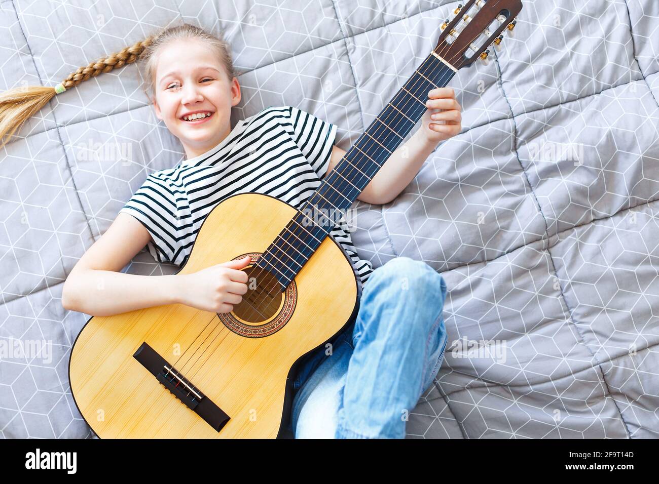 Bonne fille jouant de la guitare acoustique à la maison, allongé sur le lit, vue du dessus. Banque D'Images