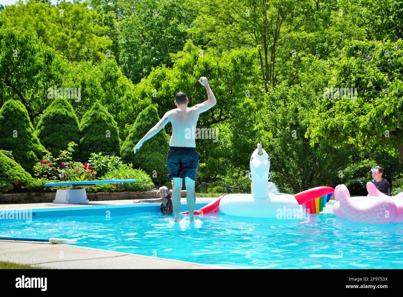 un père sautant un plongeoir dans la piscine de l'arrière-cour Banque D'Images