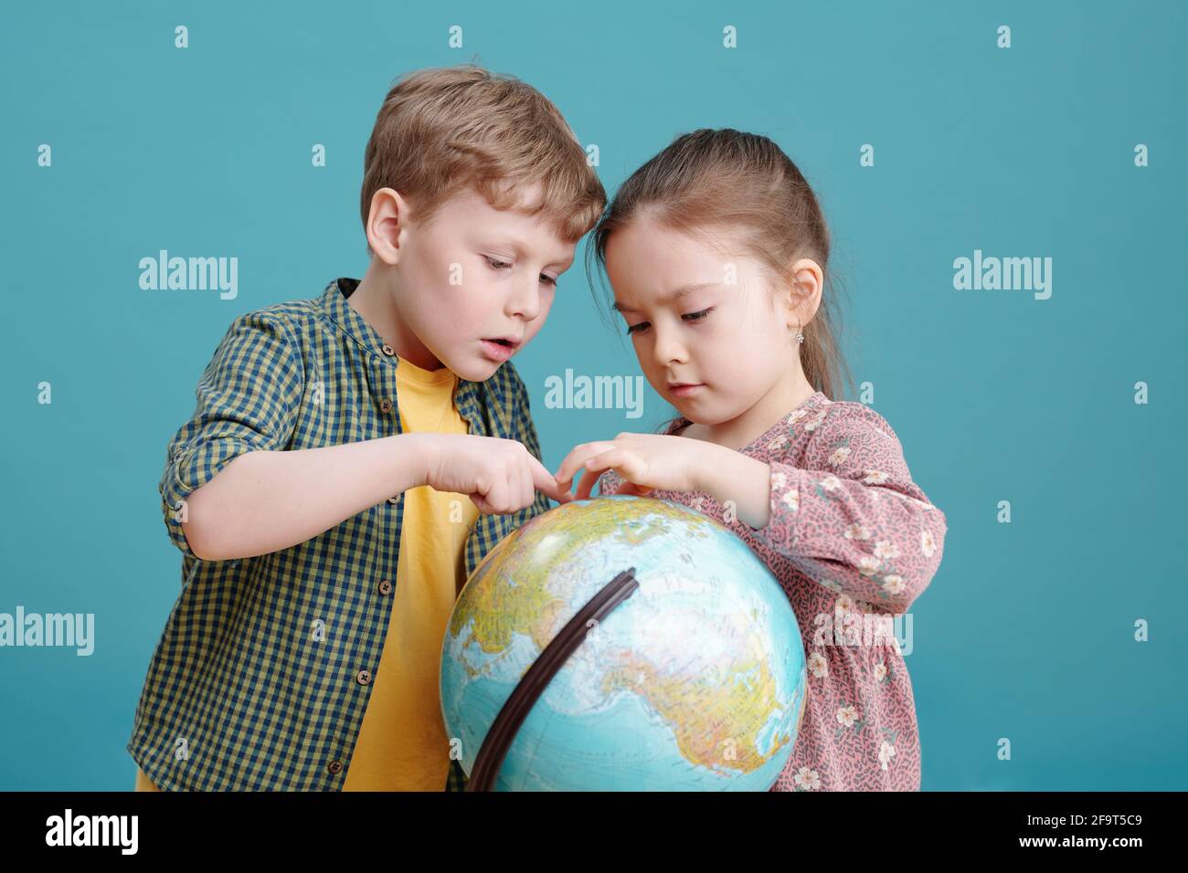 Deux petits enfants qui se tiennent debout contre le grand globe arrière-plan bleu Banque D'Images