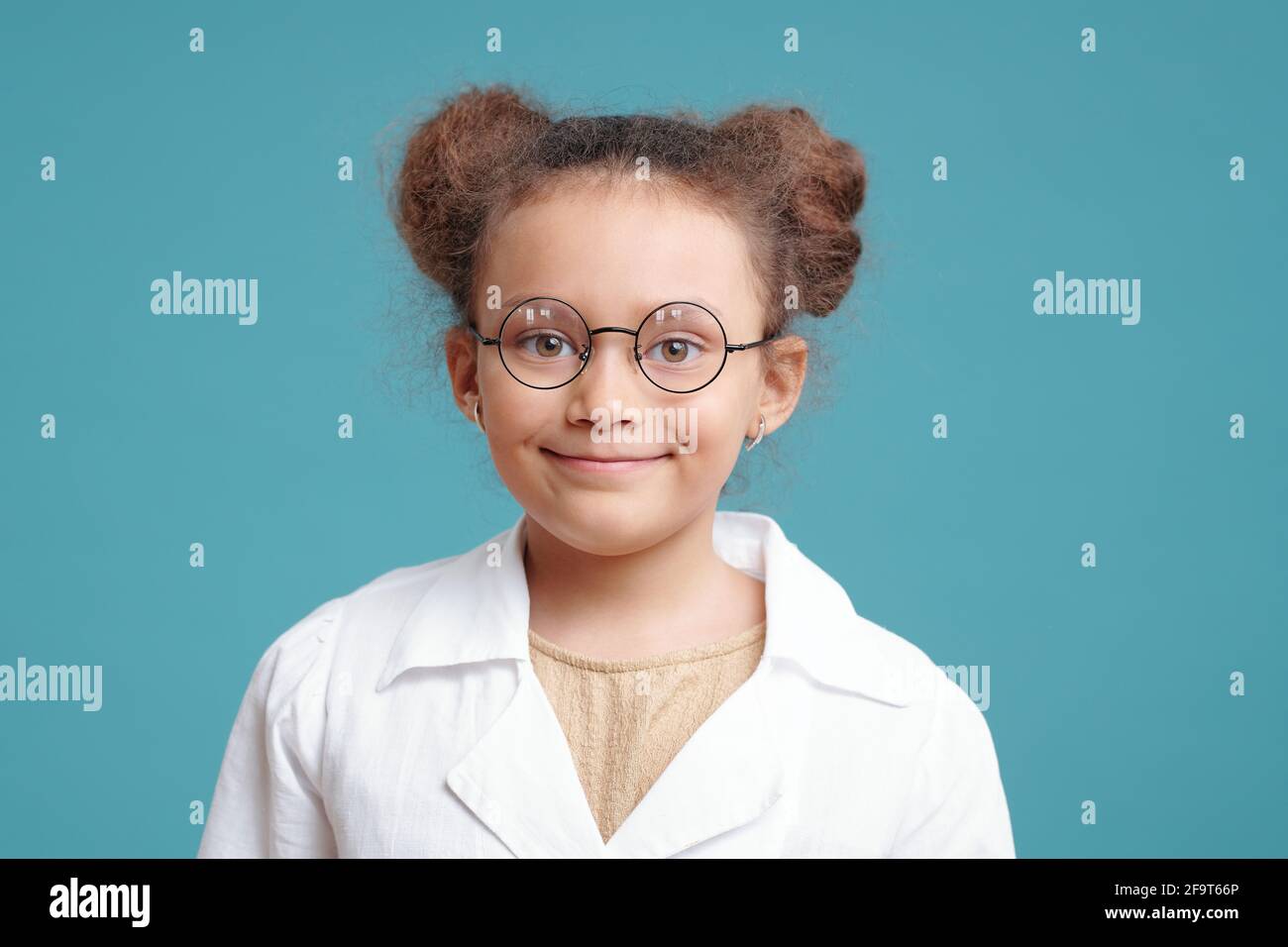 Portrait d'une petite fille mignonne en lunettes souriant à l'appareil photo sur fond bleu Banque D'Images