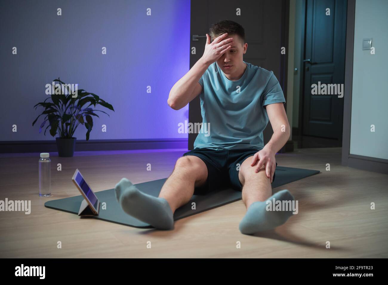 Après une séance d'entraînement à la maison dure avec l'aide d'Internet et d'une tablette, l'athlète en uniforme de sport est fatigué. Banque D'Images