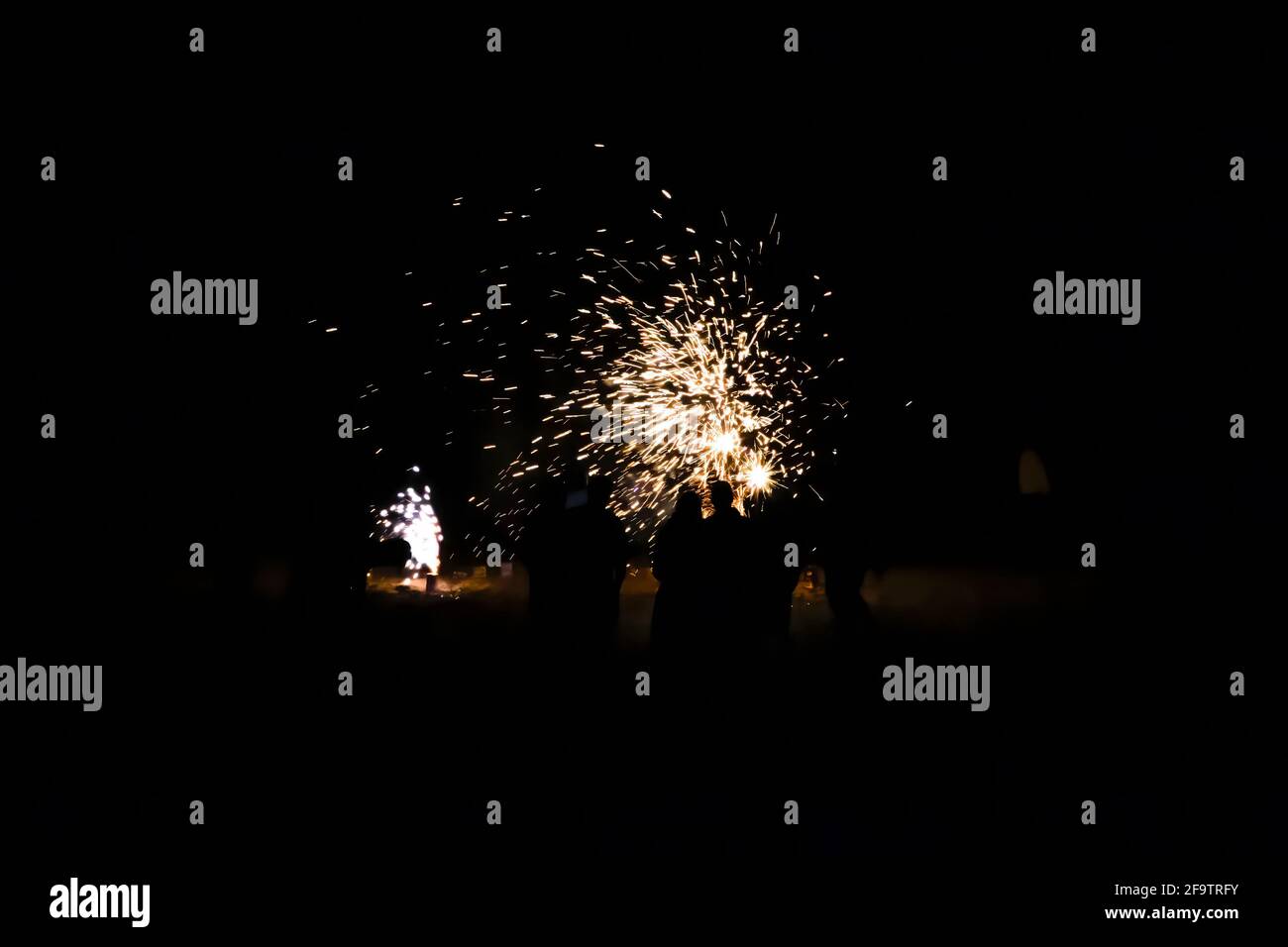 Groupe de personnes en silhouette regarder les feux d'artifice colorés exploser sur une plage la nuit. Banque D'Images