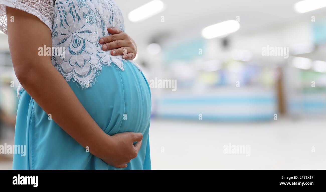 Femme enceinte vêtue d'une robe bleue sur un fond flou de l'hôpital et avoir un espace de copie. Banque D'Images