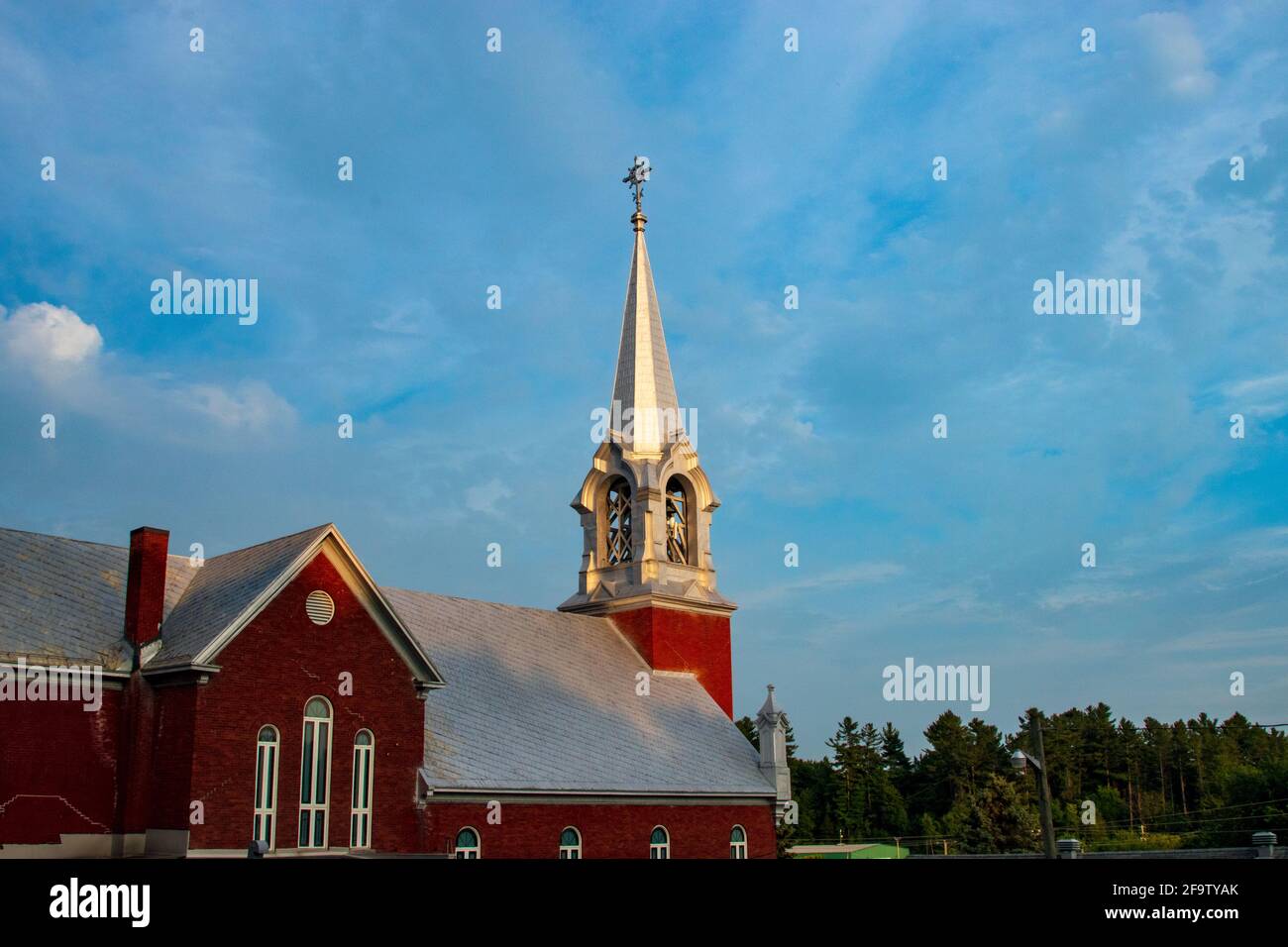 Église de campagne en brique rouge avec un clocher argenté sous un ciel bleu vif Banque D'Images
