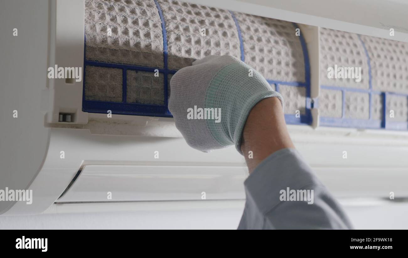 Personne qui dépose le filtre du climatiseur, main du technicien qui travaille en tirant le filtre poussiéreux du climatiseur pour le nettoyer dans la pièce à la maison Banque D'Images