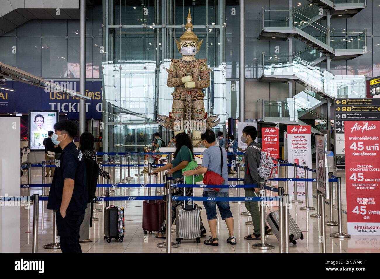 Les passagers arrivent pour un enregistrement de vol en tant que statue thaïlandaise traditionnelle portant un masque à l'aéroport de Suvarnabhumi à Bangkok, en Thaïlande, le 8 mars 2021, pendant la pandémie mondiale de covid-19. Banque D'Images