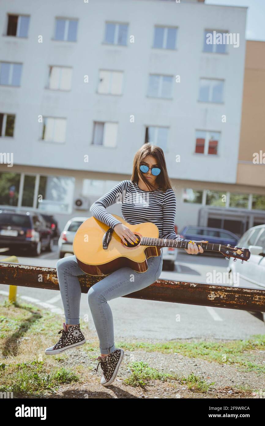 Foyer peu profond d'une femme adulte jouant une guitare acoustique en étant assis sur une ancienne barrière routière Banque D'Images