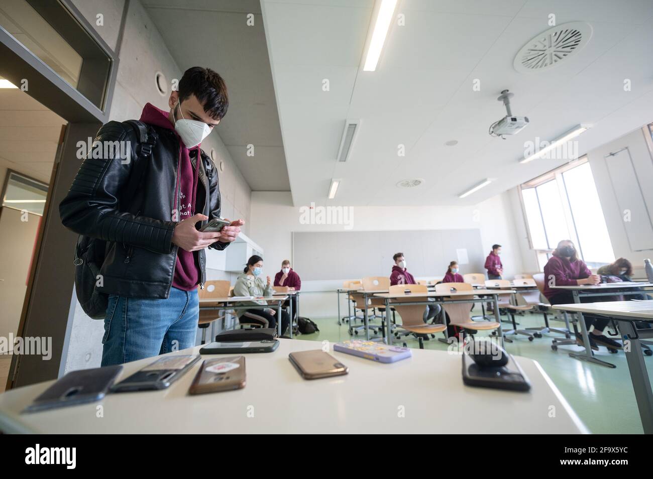 21 avril 2021, Hessen, Groß-Gerau : un étudiant portant un masque médical éteint son smartphone dans une salle de classe le premier jour des examens Abitur à l'école Prälat Diehl. Les examens commencent par la chimie du sujet et se déroulent en petits groupes. Photo: Sebastian Gollnow/dpa Banque D'Images