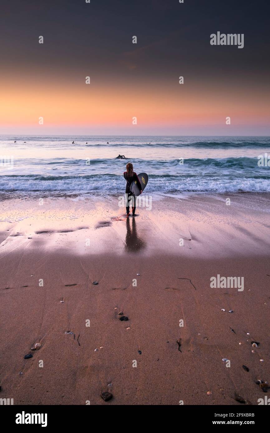 Une surfeuse femelle debout sur le rivage à la lumière du soir sur la plage de Fistral à Newquay, dans les Cornouailles. Banque D'Images