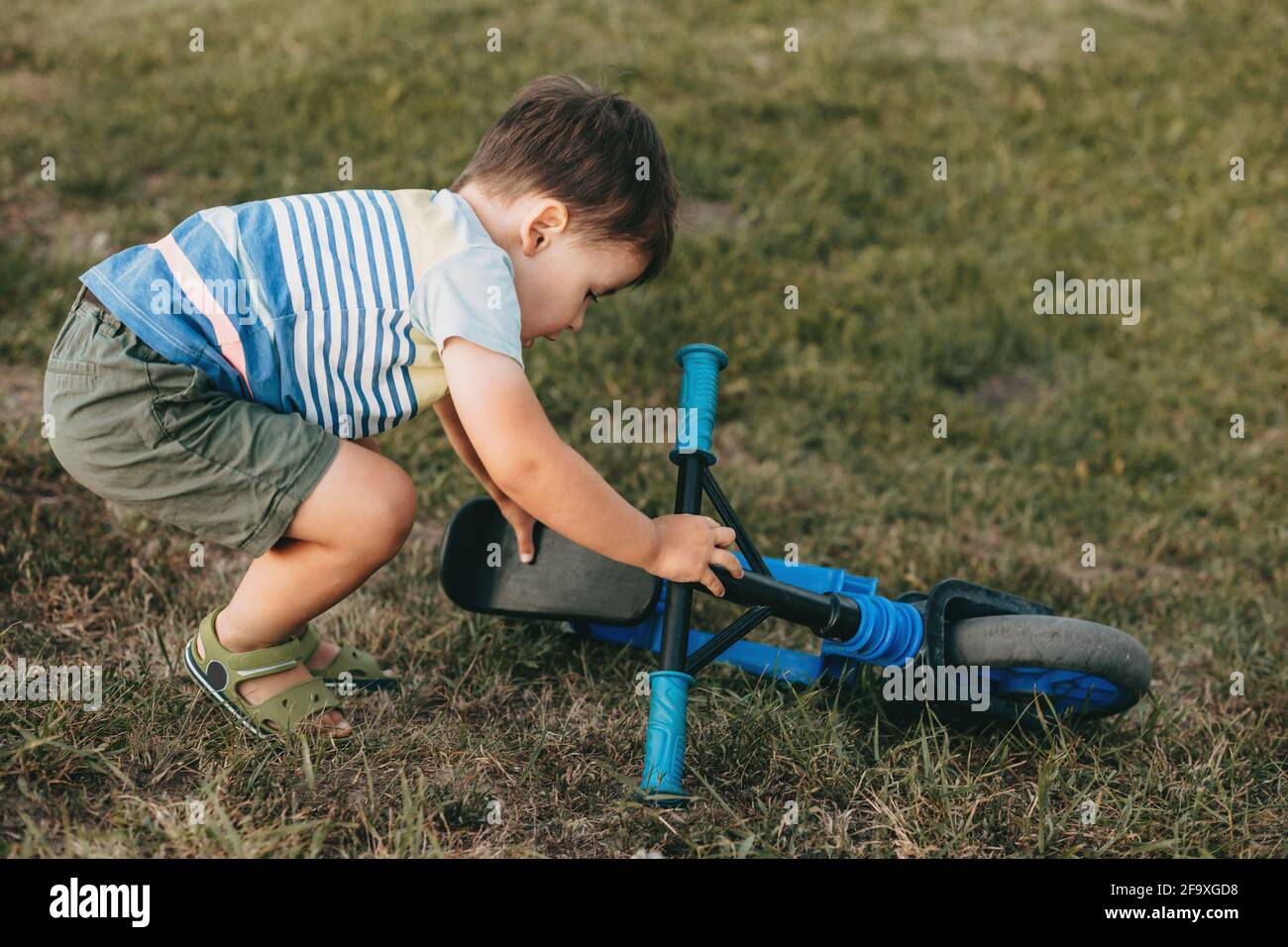 Le petit garçon caucasien est de monter le vélo après la chute dans un champ sur l'herbe Banque D'Images