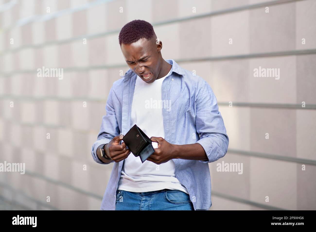 Un homme américain africain désespéré qui regarde son portefeuille vide  près de chez lui mur de briques sur la rue de la ville Photo Stock - Alamy