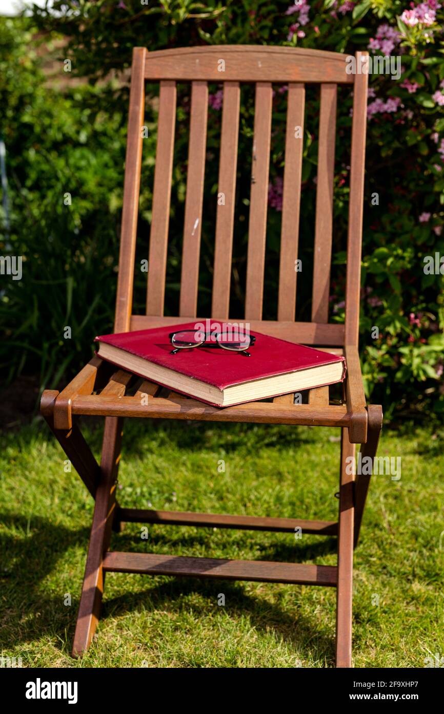 Un grand livre de couverture rigide reposant sur une chaise avec une paire de lunettes de lecture placées sur le dessus. Lecture en extérieur concept Banque D'Images