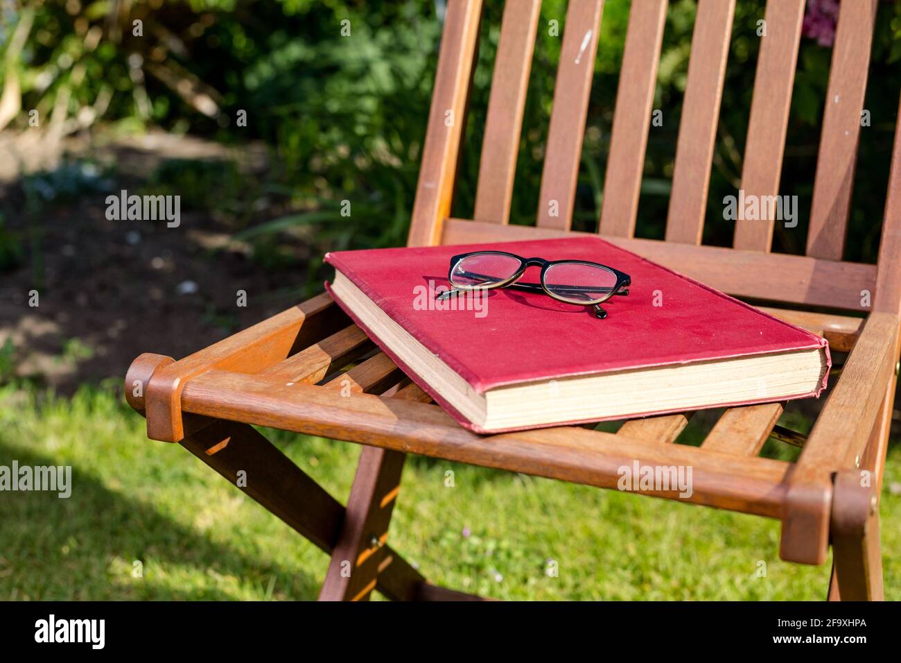 Un grand livre de couverture rigide reposant sur une chaise avec une paire de lunettes de lecture placées sur le dessus. Lecture en extérieur concept Banque D'Images