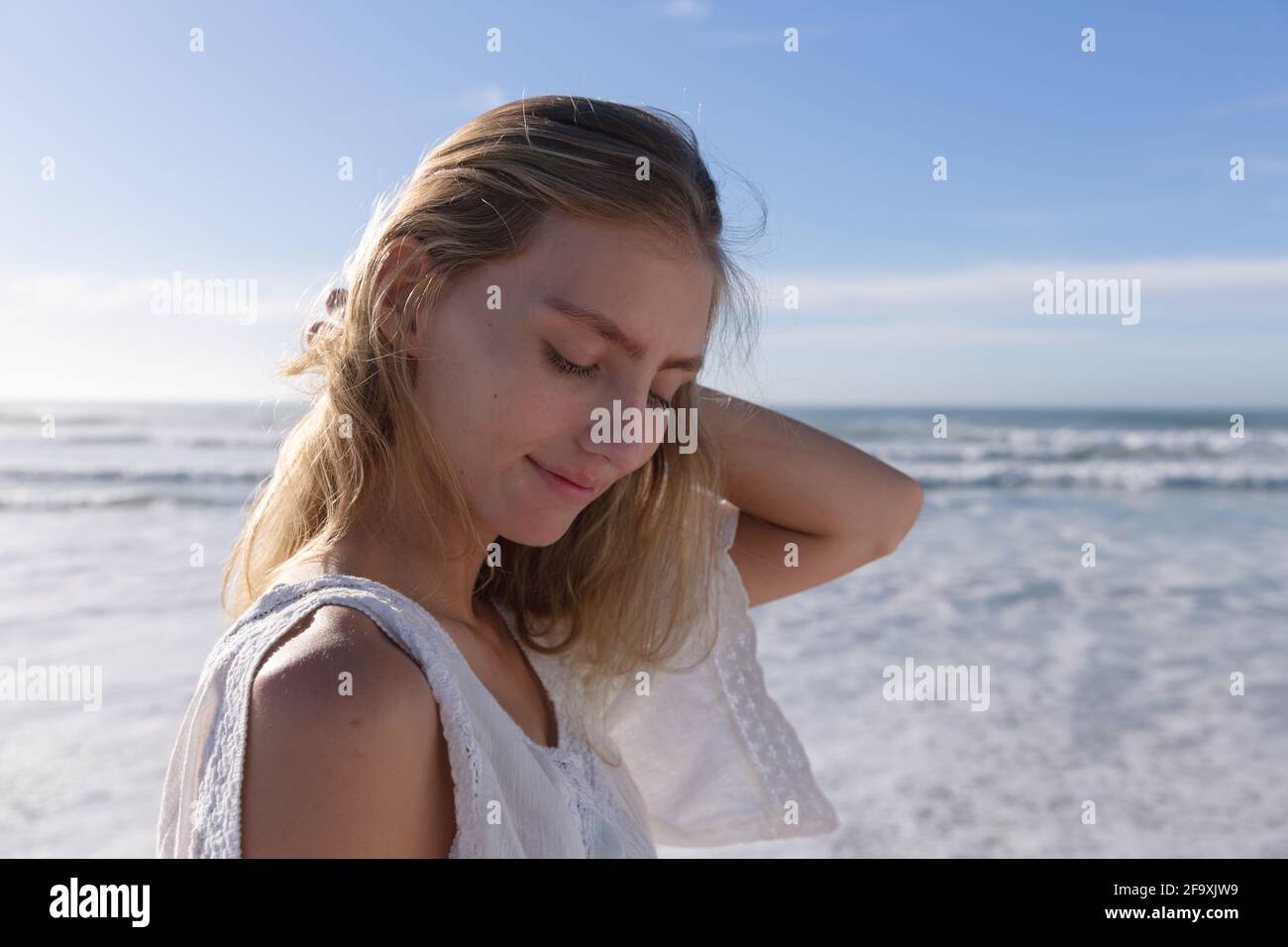Femme caucasienne souriante debout avec les yeux fermés à la plage Banque D'Images