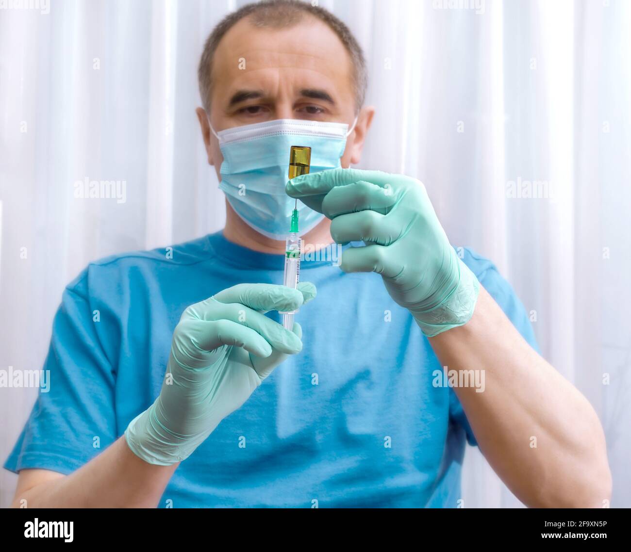 Mains d'un médecin en gants bleus avec une seringue et une bouteille de vaccin ou de médicament sur un flou arrière-plan d'un homme dans un masque Banque D'Images