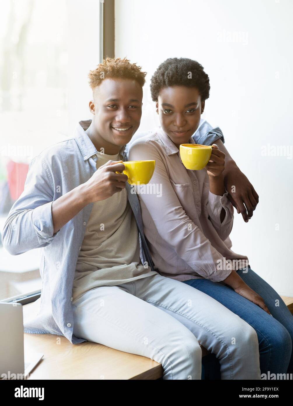 Couple noir positif assis sur le rebord de la fenêtre et buvant du café aromatique au café Banque D'Images