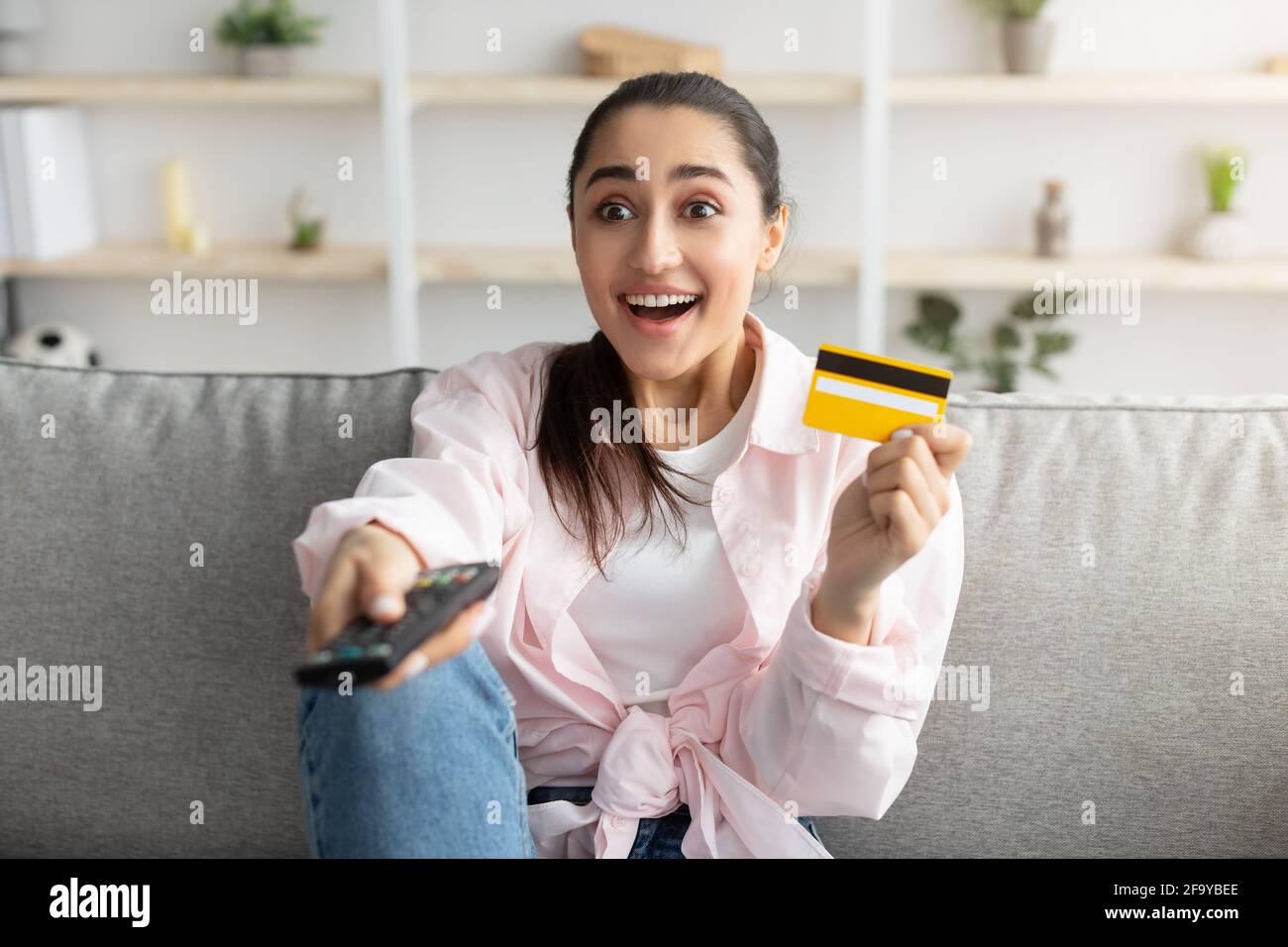 Femme excitée tenant la télécommande et la carte de crédit de débit Banque D'Images