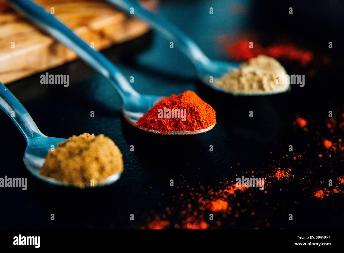 Herbes et épices colorées sur des cuillères argentées sur fond noir. Paprika, cumin, gingembre. Ingrédients pour cuisiner des aliments épicés Banque D'Images