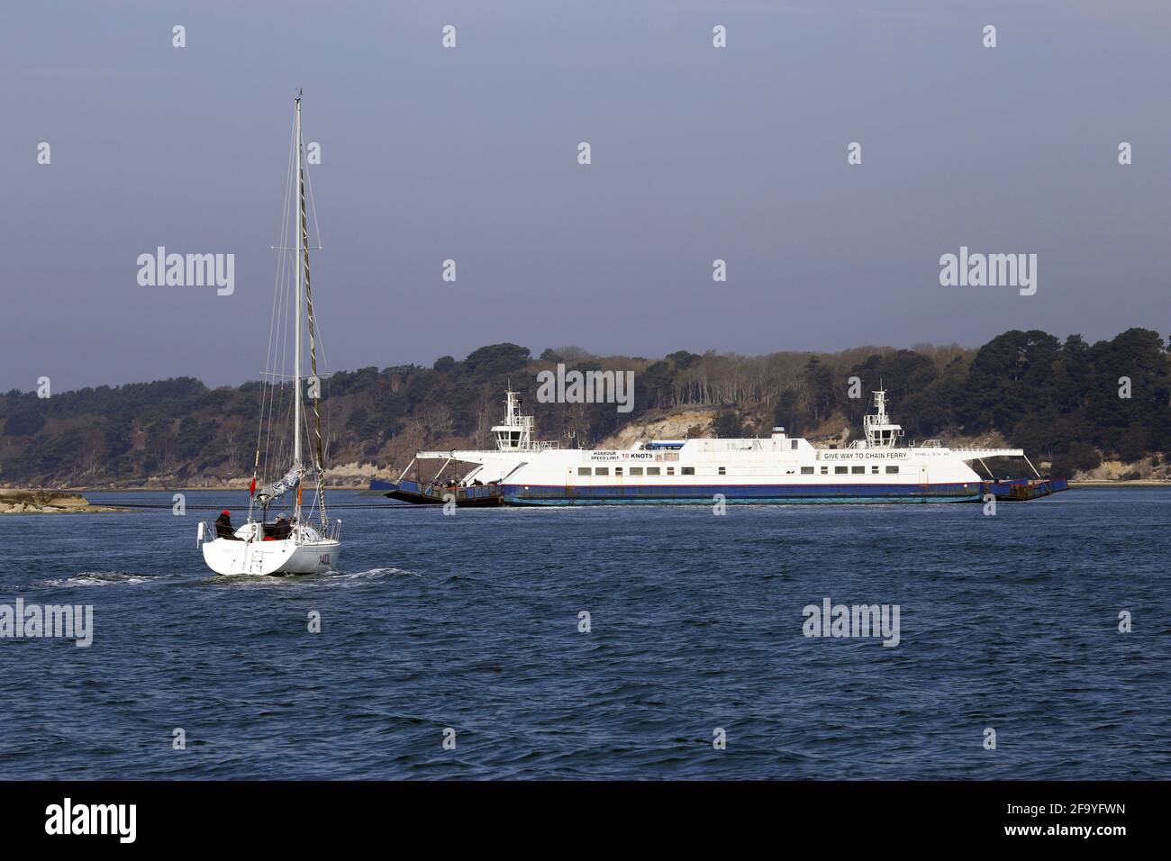 Bateau à voile approchant l'entrée du port de Poole avec le chaîne de ferry traversant l'entrée Banque D'Images