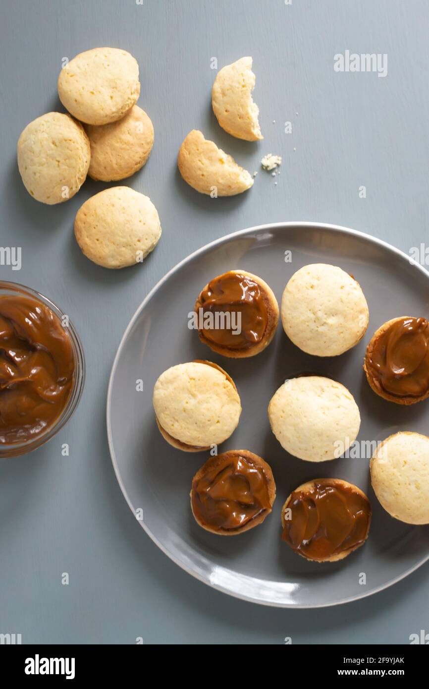 Biscuits Alfahores sur une assiette grise sur fond gris avec du lait condensé dans un bol en verre. Biscuits maison traditionnels. Concept de cuisine maison. Hori Banque D'Images