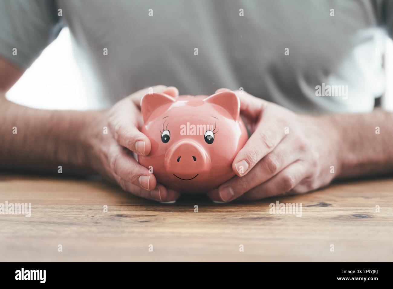 vue rapprochée de l'homme tenant une banque de porc avec les deux mains à une table en bois, économie d'argent et concept de finance Banque D'Images