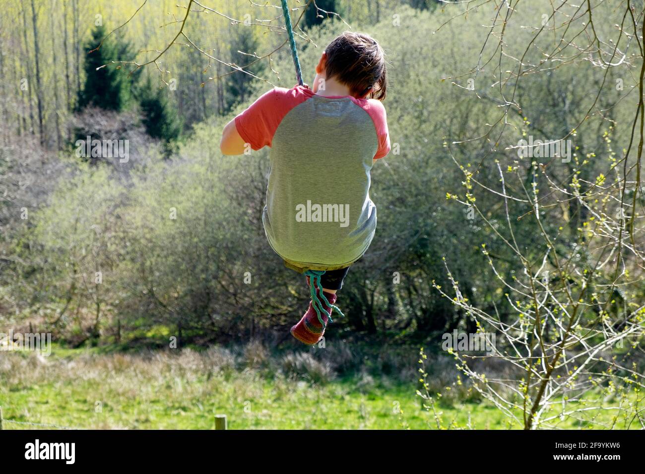 Vue arrière du garçon enfant 11 sur une balançoire de jardin après avoir facilité la vue de verrouillage dans la campagne paysage de printemps Carmarthenshire pays de Galles Royaume-Uni KATHY DEWITT Banque D'Images