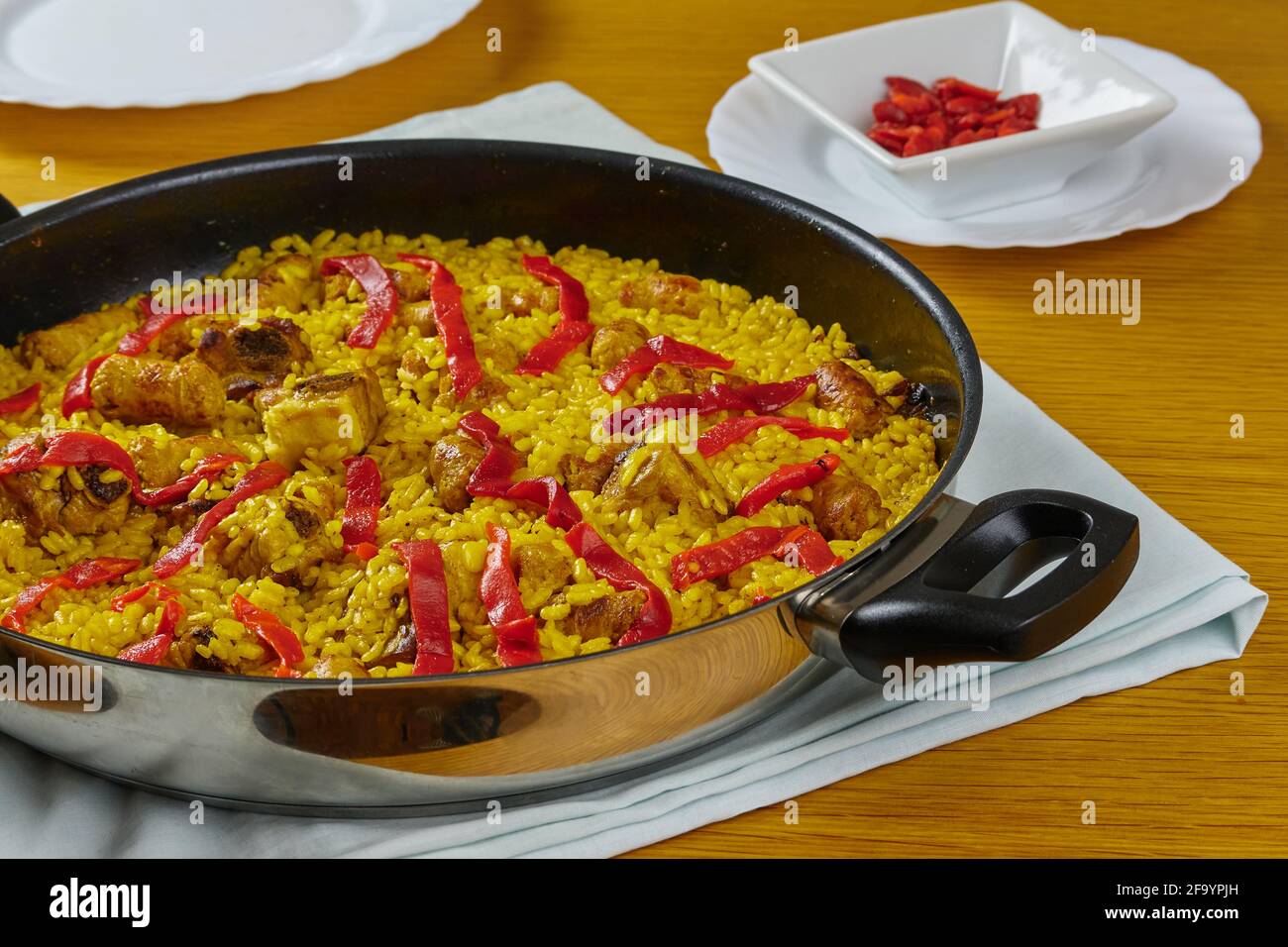 Paella traditionnelle espagnole de fruits de mer avec saucisses de porc, côtes de porc et poivrons rouges dans une poêle décorée d'une assiette de poivre rouge et d'une cuillère. Banque D'Images