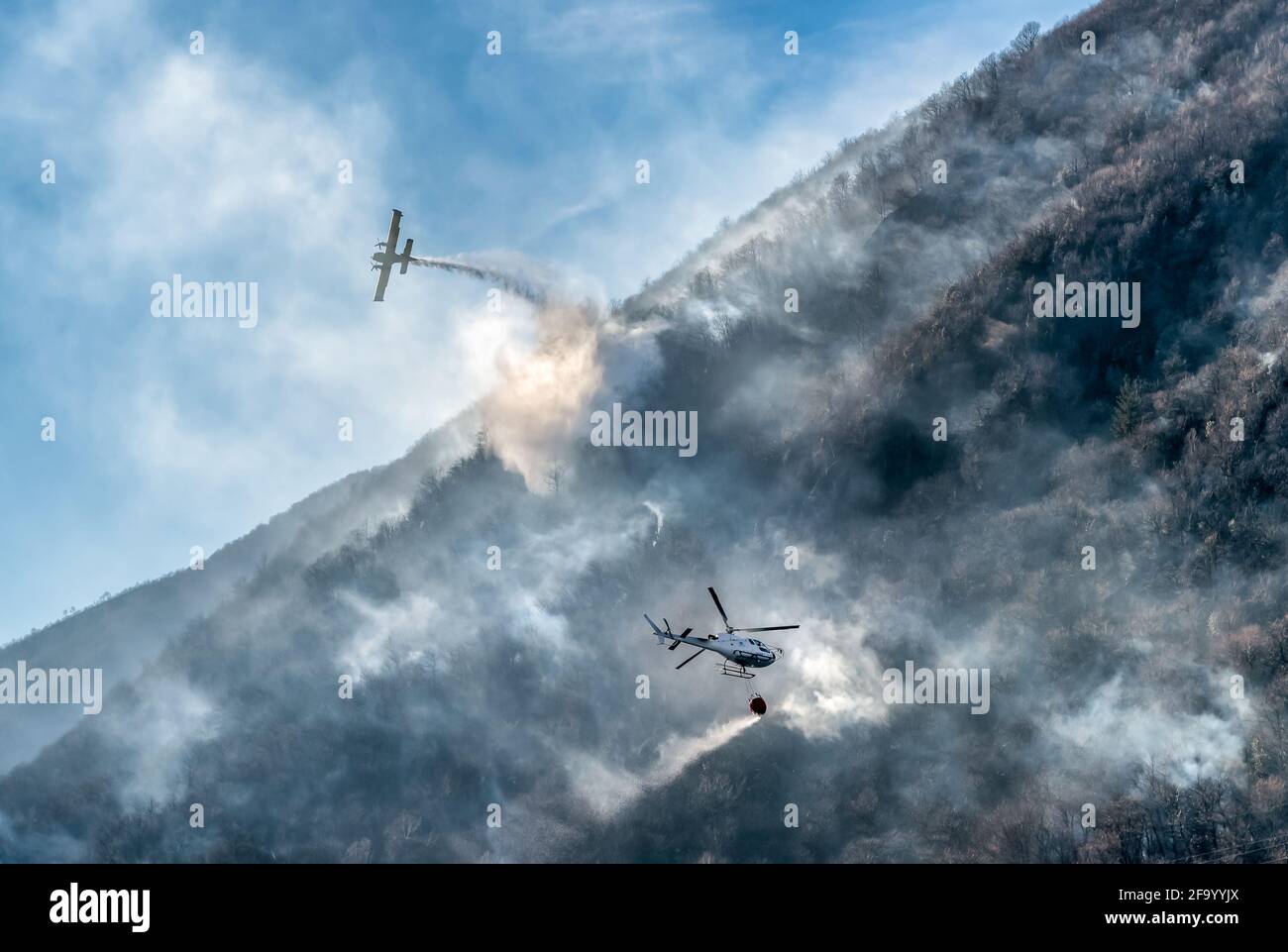 Avion de lutte contre l'incendie et hélicoptère qui larme l'eau pour combattre un incendie en montagne, au-dessus du lac Ghirla à Valganna, province de Varese, Italie Banque D'Images