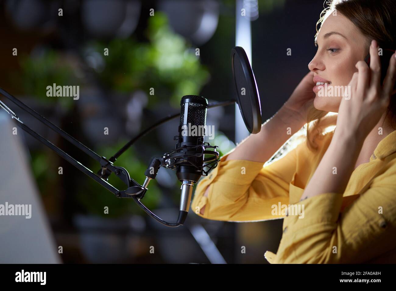 Portrait de la belle jeune femme en chemise jaune et casque moderne chantant dans un microphone noir. Concept de processus d'enregistrement de chansons modernes et à la mode dans un studio professionnel. Banque D'Images