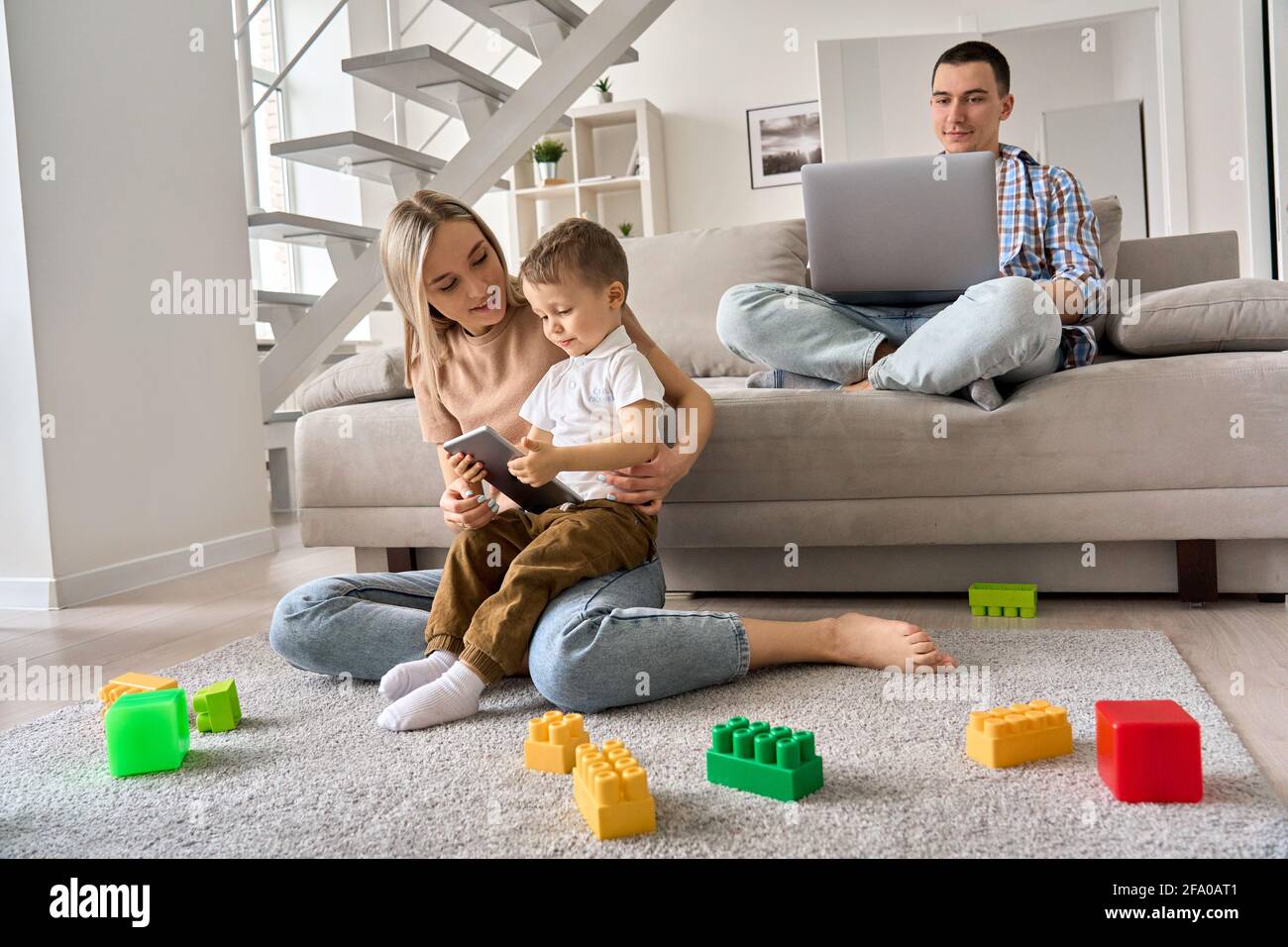 Jeune famille à la maison, maman et enfant regardant des vidéos sur tablette, papa travaillant sur pc. Banque D'Images