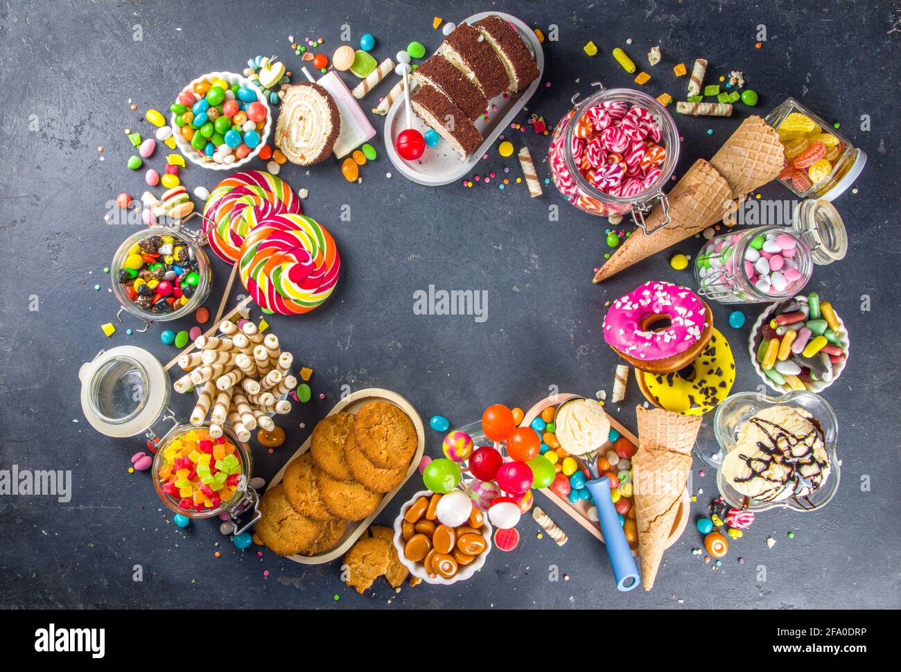 Sélection de bonbons colorés. Assortiment de bonbons, chocolats, beignets, biscuits, sucettes, vue sur le dessus de la glace sur fond de béton noir Banque D'Images