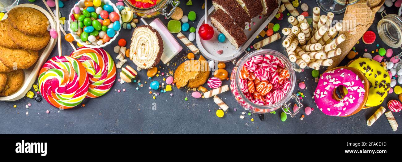 Sélection de bonbons colorés. Assortiment de bonbons, chocolats, beignets, biscuits, sucettes, vue sur le dessus de la glace sur fond de béton noir Banque D'Images