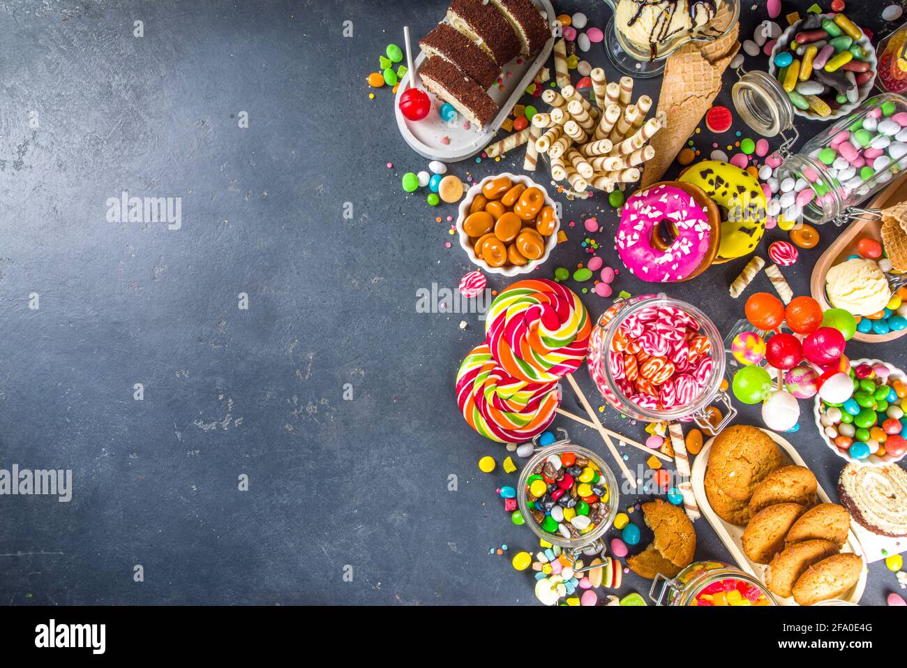 Sélection de bonbons colorés. Assortiment de bonbons, chocolats, beignets, biscuits, sucettes, vue sur le dessus de la glace sur fond de béton noir Banque D'Images