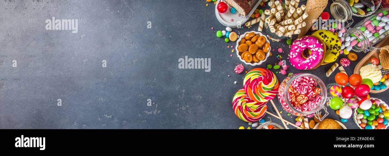 Sélection de bonbons colorés. Assortiment de bonbons, chocolats, beignets, biscuits, sucettes, vue sur le dessus de la glace sur fond de béton noir Banque D'Images