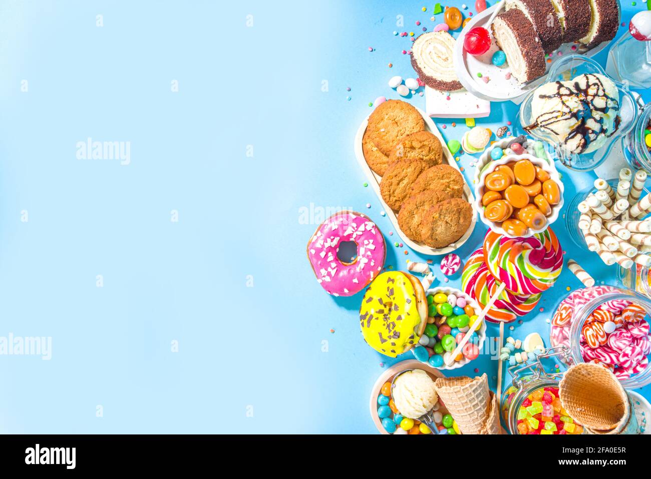 Sélection de bonbons colorés. Assortiment de bonbons, chocolats, beignets, biscuits, sucettes, vue sur le dessus de crème glacée sur le fond de soungroun ensoleillé bleu vif tendance Banque D'Images