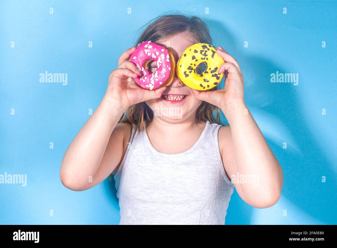 Petite fille drôle heureuse avec sucre coloré glacé de beignets roses et jaunes, vacances, bonheur, concept de vacances d'été, Banque D'Images