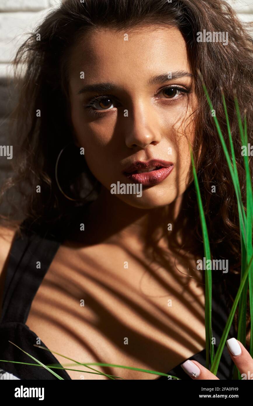 Portrait de jeune femme brune attrayante avec maquillage tendance posant avec des feuilles vertes dans l'humeur sensuelle. Concept de prise de vue professionnelle dans une bonne atmosphère. Banque D'Images