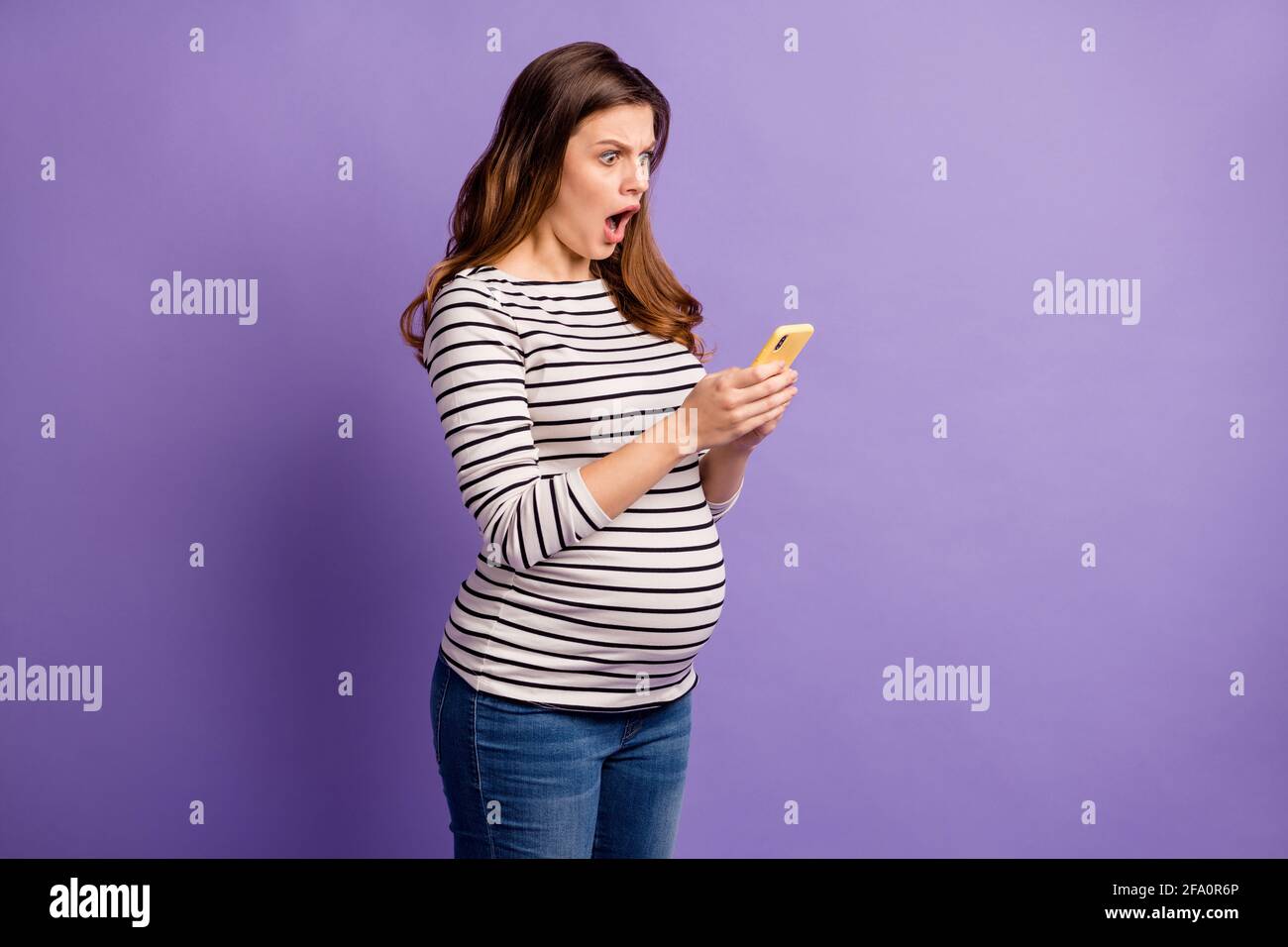 Photo De La Femme Choquee S Attendant A L Enfant Porter Une Chemise Rayee Ventre Dispositif Moderne De Dactylographie A Bouche Ouverte Fond Violet Isole Photo Stock Alamy