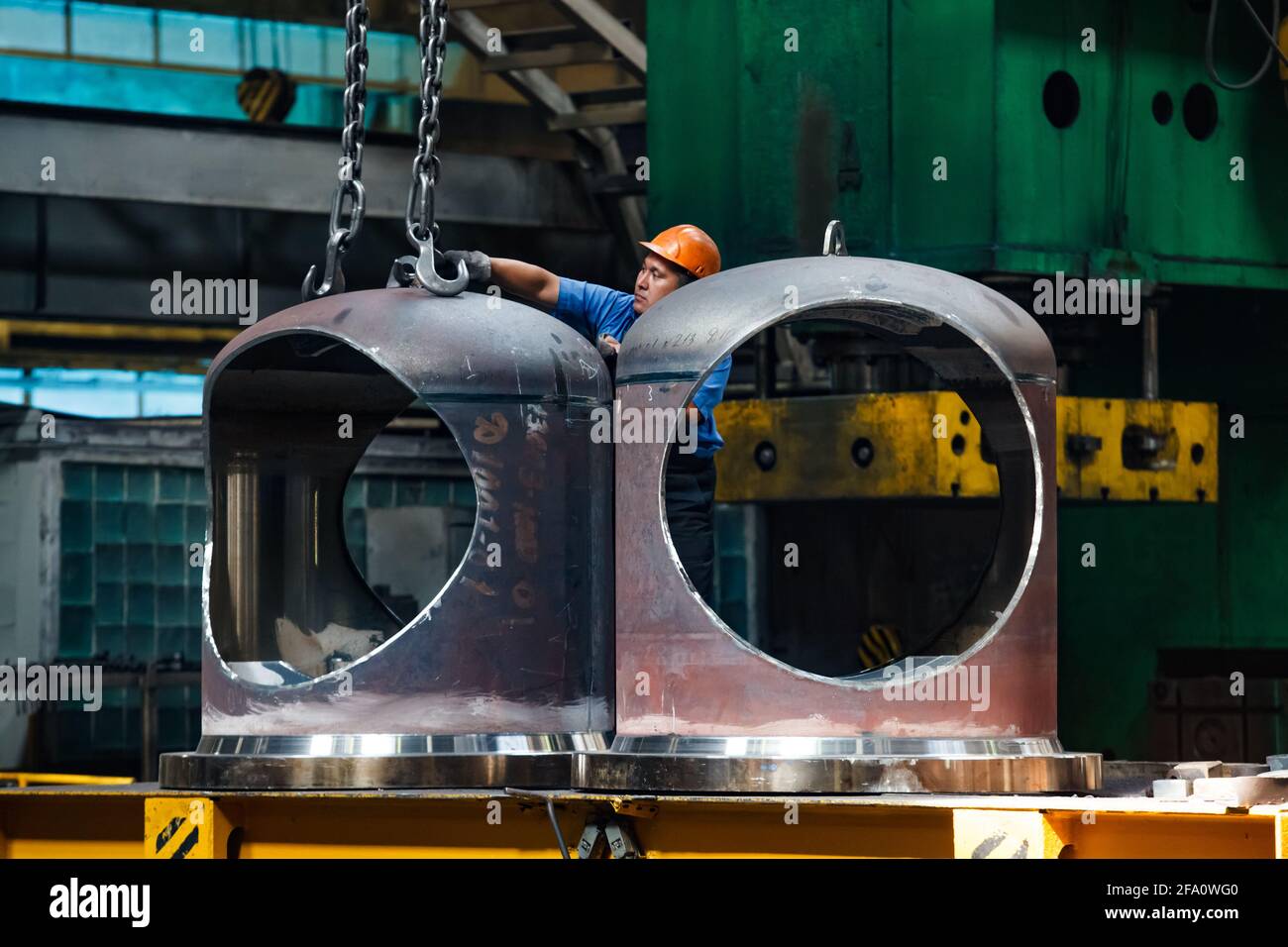 Un travailleur asiatique en casque orange lève la valve géante par grue,  chaîne et crochet. Usine de fabrication de vannes d'arrêt pour l'industrie  du pétrole et du gaz Photo Stock - Alamy